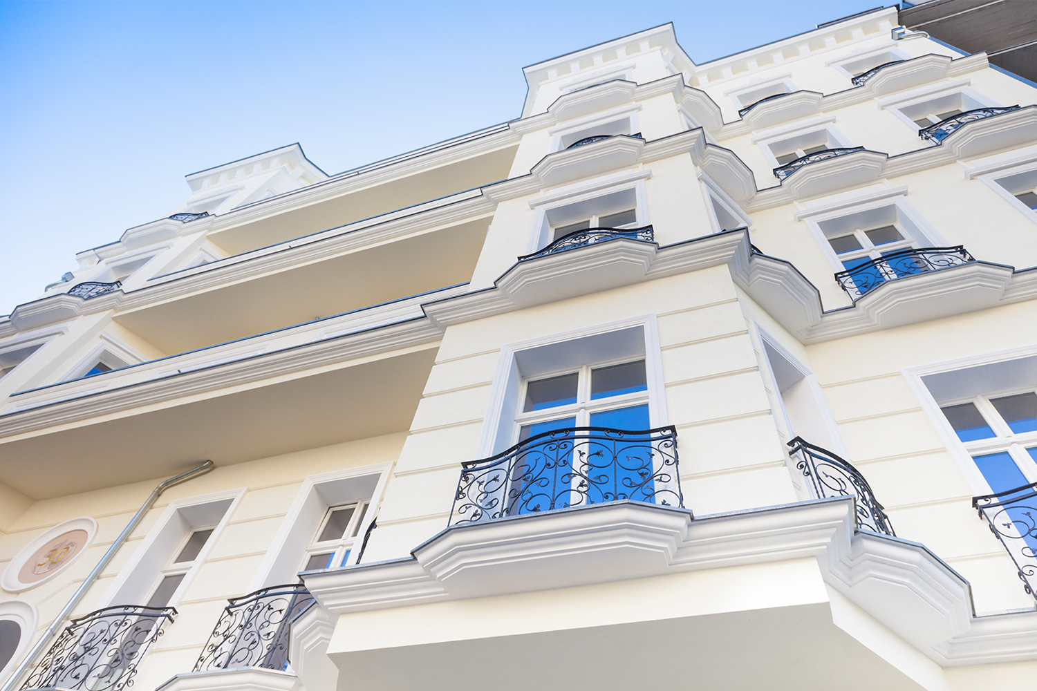 „Renovierte Fassade eines mehrgeschossigen Wohngebäudes mit hellcremer Putzoberfläche, weißen Fenstern und schwarzen Schmiedeeisen-Balkonen – hochwertige Fassadengestaltung vom Malerfachbetrieb Binder.“