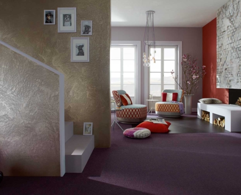 Wohnraum mit metallisch schimmernder Spachteltechnik, rosé-grauen Wandflächen, roter Kaminwand und strukturierter Putzoberfläche – gestaltet vom Malerfachbetrieb